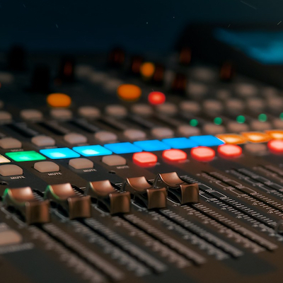 close-up shot of an audio mixing board with buttons, faders and color lights