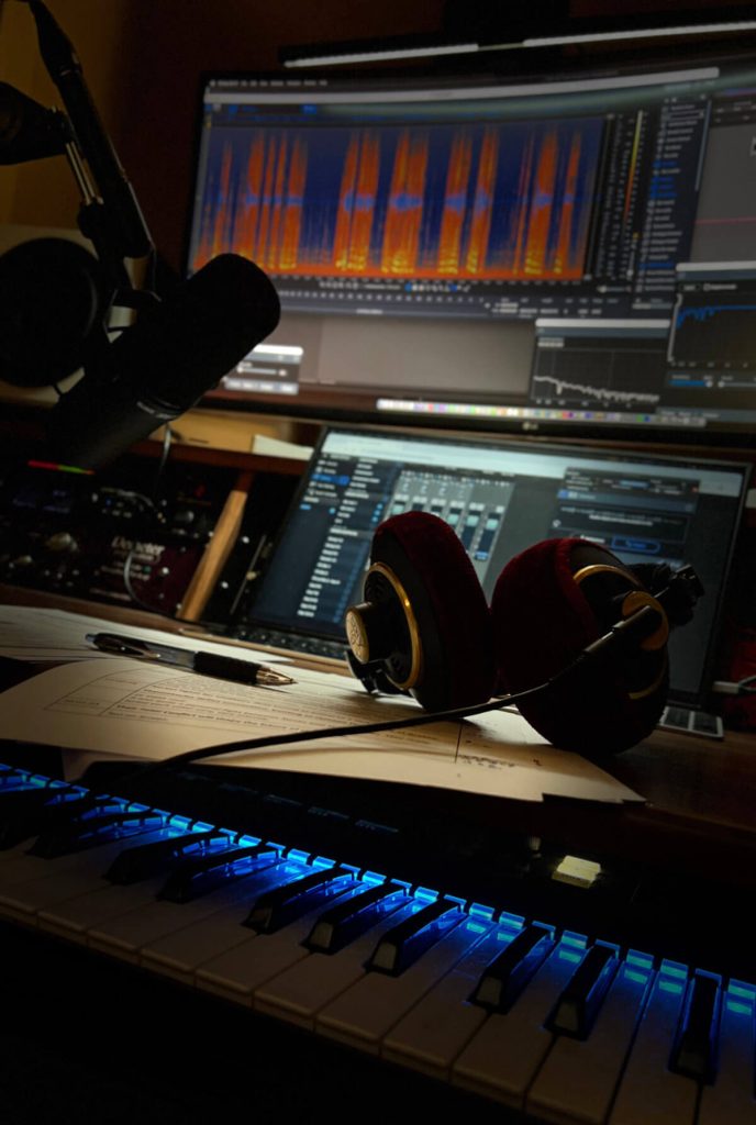 Voiceover studio desk with waveform editing software, headphones, and keyboard illuminated in warm light.